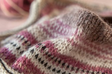 Pembe beton arka planda sıcak çizgili paçavra süveter parçası. Örgü örme işlemleri, alpaka, farklı renkte iplikler. Hygge rahat bir zanaat atmosferi. Yumuşak odak