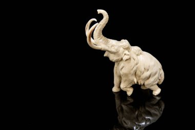 Fildişi mamut heykelciği siyah arkaplanda yansımalı. Eski kemikten bir oymayla oyulmuş. İç mekan için otantik dekoratif figür.
