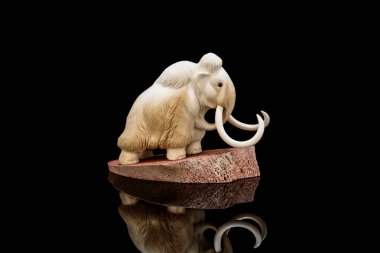 Fildişi mamut heykelciği siyah arkaplanda yansımalı. Eski kemikten bir oymayla oyulmuş. İç mekan için otantik dekoratif figür.