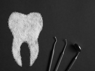 Sugar harms the tooth enamel. Image of a sugar tooth with medical instruments on a black background. Concept of dental medicine. clipart