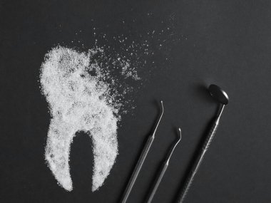 Sugar harms the tooth enamel. Image of a sugar tooth with medical instruments on a black background. Concept of dental medicine. clipart