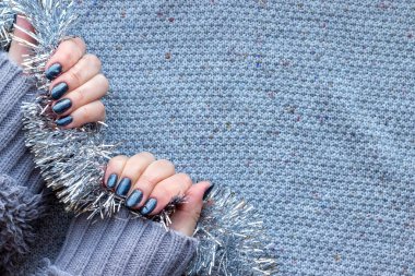 Gri örgü süveterli, güzel manikürlü kadın elleri. Arka planda koyu gri, parlak çiviler. Fotokopi alanı olan gümüş Noel süsleri.