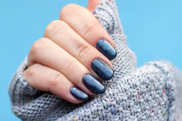 女性的手在灰色针织毛衣面料与美丽的指甲 深灰色的蓝色闪光的指甲蓝色背景 有选择的重点 闭包视图 — 图库照片