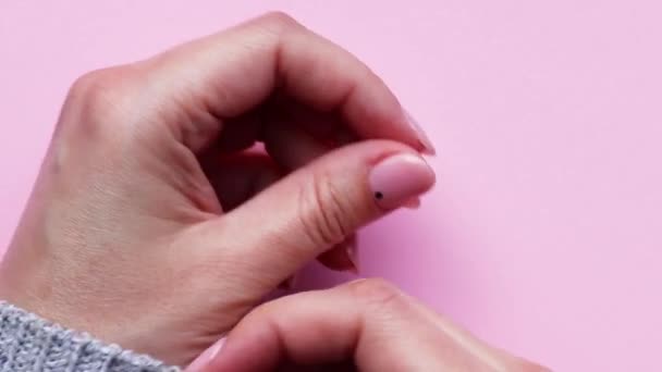Mains féminines avec une belle manucure tendance - ongles nus roses avec de petits points noirs enveloppés dans un pull gris tricoté sur un fond rose — Video