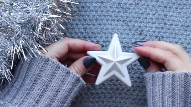 Žena ruce s lesklými nehty v šedém svetru rotující bílé vánoční stromeček hračka hvězda na pleteném pozadí se stříbrnou tinsel girland — Stock video