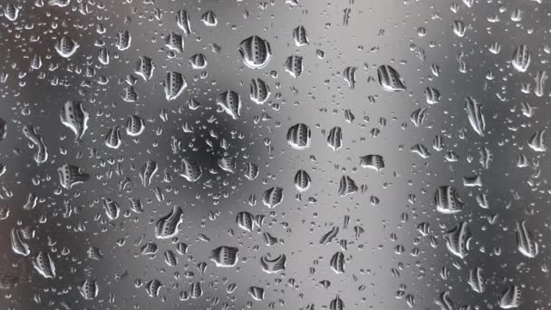 Dešťové kapky padající na okenní sklo na rozmazaném pozadí domu v deštivém oblačném dni. Kapky různých velikostí odrážejí sousední bytový dům — Stock video