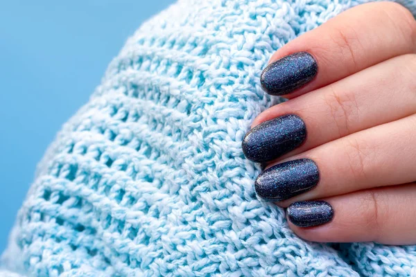 Ręka kobiety z dzianiny sweter tkaniny z pięknym manicure - granatowe błyszczące paznokcie na niebieskim tle. Wybiórcze skupienie. Widok z bliska — Zdjęcie stockowe