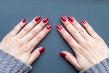 Güzel manikürlü kadın eli. Gri arka planda kırmızı parıldayan tırnaklar.