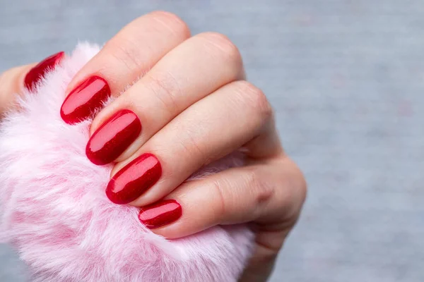 Female hand with pink fluffy ball with beautiful manicure - red glittered nails. Selective focus. Closeup view — Stock Photo, Image