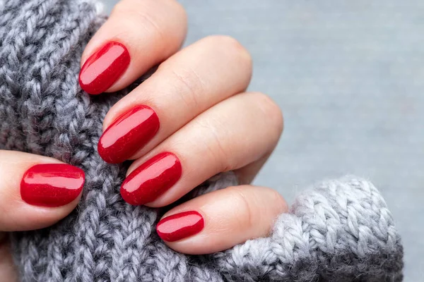 Weibliche Hand mit grauem Strickschal mit schöner Maniküre - rot glitzernde Nägel. Selektiver Fokus. Nahaufnahme — Stockfoto