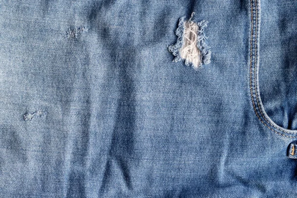 Azul rasgado jeans textura de tecido. Denim angustiado com buraco e fundo de bolso — Fotografia de Stock