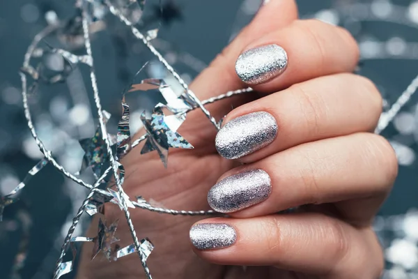 Vrouwelijke hand met mooie vakantie manicure - zilveren glitternagels met kerst gedraaide draad met sterren. Selectieve focus. Van dichtbij gezien. wazig grijze achtergrond — Stockfoto