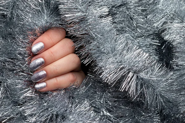 Vrouwelijke hand met mooie vakantie manicure - zilver glitterde nagels op kerst tinsel achtergrond met kopieerruimte — Stockfoto