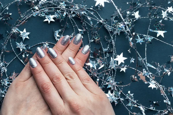 Weibliche Hände mit schöner Feiertagsmaniküre - silber glitzernde Nägel mit weihnachtlichem Draht mit Sternen auf grauem Hintergrund. Selektiver Fokus. Nahaufnahme — Stockfoto