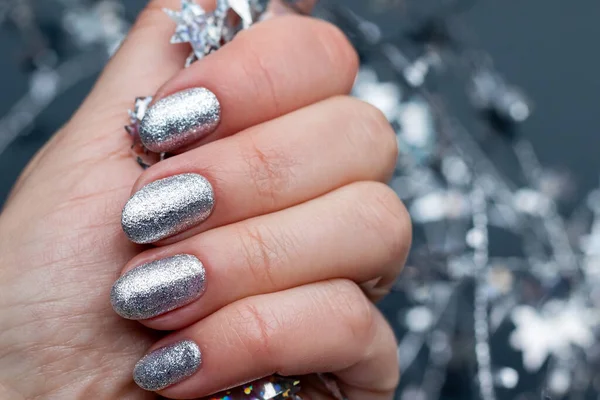 Kobieca ręka z pięknym wakacyjnym manicure - srebrne błyszczące paznokcie ze świątecznym skręconym drutem z gwiazdami. Wybiórcze skupienie. Widok z bliska. Zamazane szare tło — Zdjęcie stockowe