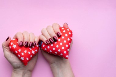 Güzel manikürlü kadın elleri. Pembe arka planda koyu kırmızı tırnaklar. İki yumuşak kırmızı kalp ve kopyalama alanı var.