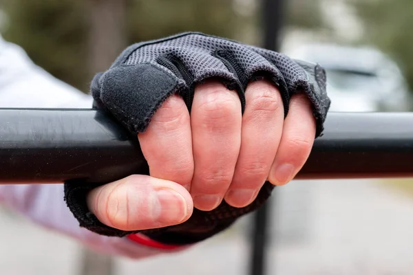 Male hand in a sports glove closeup on the horizontal bar outdoors. Selective focus