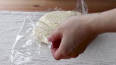 Ahşap bir masanın üzerindeki keten bir masa örtüsüne çiğ krem hamuru naylona saran eller. Ekmek ya da kruvasan yapma süreci