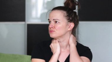 Boynunda ağrı hisseden bir kadın cerrahi tasma takıyor ve bulanık bir arka plana karşı evinde gülümsüyor.