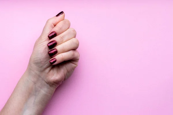 Mano femenina con hermosa manicura - uñas brillantes de color rojo oscuro sobre fondo rosa con espacio para copiar — Foto de Stock