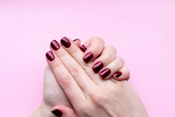 Las manos femeninas con la manicura hermosa - las uñas rojas oscuras brillantes sobre el fondo rosado — Foto de Stock