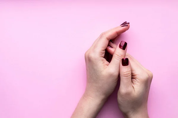 Female hands with beautiful manicure - dark red glittered nails on pink background with copy space — Stock Photo, Image