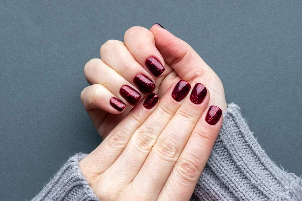 Manos femeninas en tejido suéter de punto gris con hermosa manicura - uñas brillantes de color rojo oscuro sobre fondo gris —  Fotos de Stock