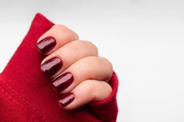 Kvinnlig hand i röd tröja med vacker manikyr - mörkröda glittrande naglar på vit bakgrund med kopieringsutrymme. Selektivt fokus. Närbild — Stockfoto