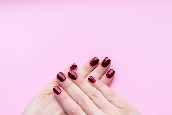 Жіночі руки з красивим манікюром - темно-червоні блискітки нігтів на рожевому фоні з пробілом для копіювання — стокове фото