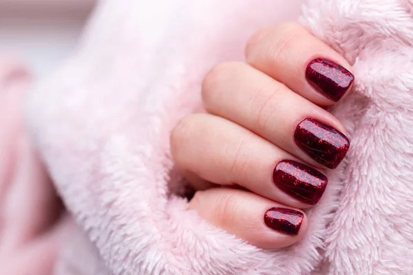 Женская рука с красивым маникюром - темно-красные блестящие ногти на розовой пушистой ткани, текстильный фон с копировальным пространством. Селективный фокус — стоковое фото