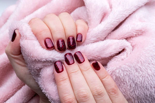 Las manos femeninas con la manicura hermosa - las uñas oscuras rojas brillantes con la tela rosada esponjosa, textil. Enfoque selectivo —  Fotos de Stock