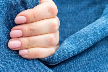 Güzel manikürlü bir kadın eli. Kot pantolon tekstil arka planında pembe çıplak tırnaklar.