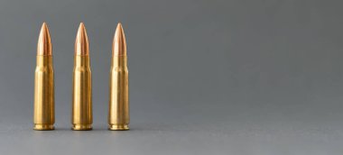 Gri arka planda üç kurşun. Kalaşnikof taarruz tüfeği için 7.62 kalibrelik fişekler, kopyalama alanı olan yakın plan pankart.