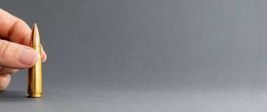 Gri arka planda bir kurşunla. Kalaşnikof taarruz tüfeği için 7.62 kalibre fişek. Parmakları yakın plan geniş pankarttır.