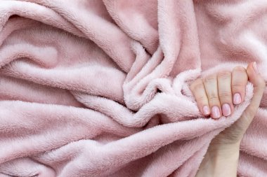 Güzel manikürlü bir kadın eli. Pembe çıplak tırnaklar, buruşuk pembe yumuşak kumaş, kopya alanı olan tekstil arka planı.