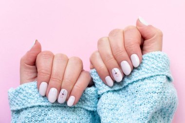 Güzel manikürlü mavi örgü süveterli kadın elleri. Pembe arka planda çiçekli beyaz fildişi tırnaklar.