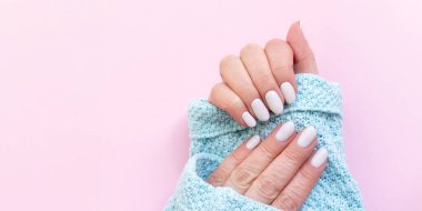 Güzel manikürlü mavi örülü kadın eli. Pembe arka planda beyaz fildişi tırnaklar. Fotokopi alanı olan şablon pankartı.