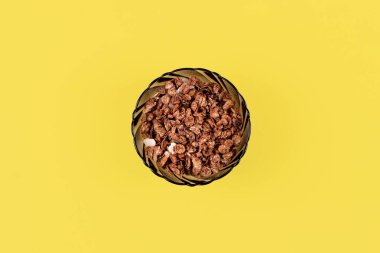 Ev yapımı organik kavrulmuş tahıl gevreği yulaf, keten, badem, sarı arka planda yuvarlak cam kasede çikolata. Üst görünüm müsli