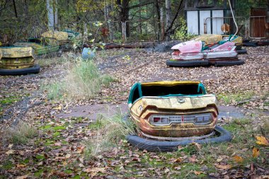 Pripyat, Çernobil Yasak Bölgesi 'ndeki eğlence parkında yosun ve sonbahar yaprakları arasında terk edilmiş eski, paslı, metal, radyoaktif sarı araba.