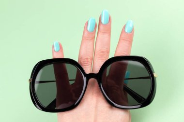 Güzel manikürlü kadın eli - yeşil arka planda güneş gözlüklü nane mavisi tırnaklar, yakın plan, seçici odaklanma