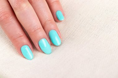 Güzel manikürlü bir kadın eli. Çuval bezi kumaş arka planında nane mavisi tırnaklar. Kopya alanı ile yakın plan. Seçici odak