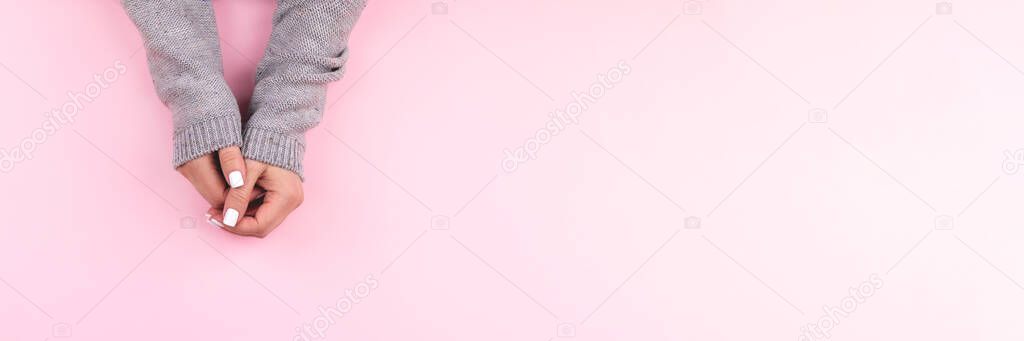 Hands in sweater with white nails on pink background