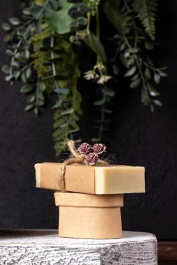 Kırsal ahşap üzerinde el yapımı sabun ve ahşap zemin üzerinde yeşil bitkiler ve siyah beton duvarlı karton podyum. Kahverengi kağıt, kenevir ipi ve kağıt çiçek paketi. Spa organik tedavi