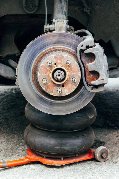 Rusty back car wheel hub with brake disc at tire shop. Car without wheel lifted on the pneumatic jack while replacing on the tire service center