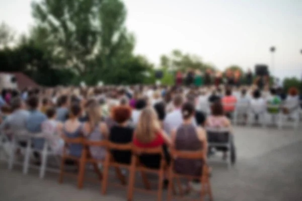 People are watching a concert of classical music. blurred young and adult women and men and other people watching listening to concert of classical band in daylight outdoor enviroment.