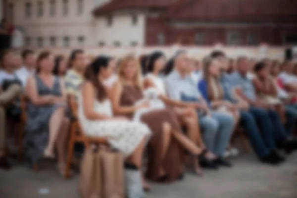 İnsanlar klasik müzik konseri izliyorlar. Bulanık genç ve yetişkin kadınlar, erkekler ve diğer insanlar klasik orkestranın konserini açık havada dinliyorlardı..