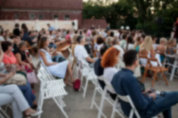 İnsanlar klasik müzik konseri izliyorlar. Bulanık genç ve yetişkin kadınlar, erkekler ve diğer insanlar klasik orkestranın konserini açık havada dinliyorlardı..