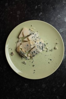 Siyah arka planda hafif tabakta küflü mavi peynir. Mavi peynir. Siyah arka planda hafif tabakta yenilebilir küflü peynir. Üst görünüm.