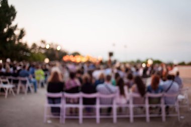 İnsanlar klasik müzik konseri izliyorlar. Bulanık genç ve yetişkin kadınlar, erkekler ve diğer insanlar klasik orkestranın konserini açık havada dinliyorlardı..