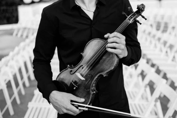 ヴァイオリニストはバイオリンを手で演奏する ヴァイオリニストはバイオリンと弓を手に持っている バイオリンを持っている男たち バイオリンを手に若い音楽家が立っている 白黒写真です — ストック写真